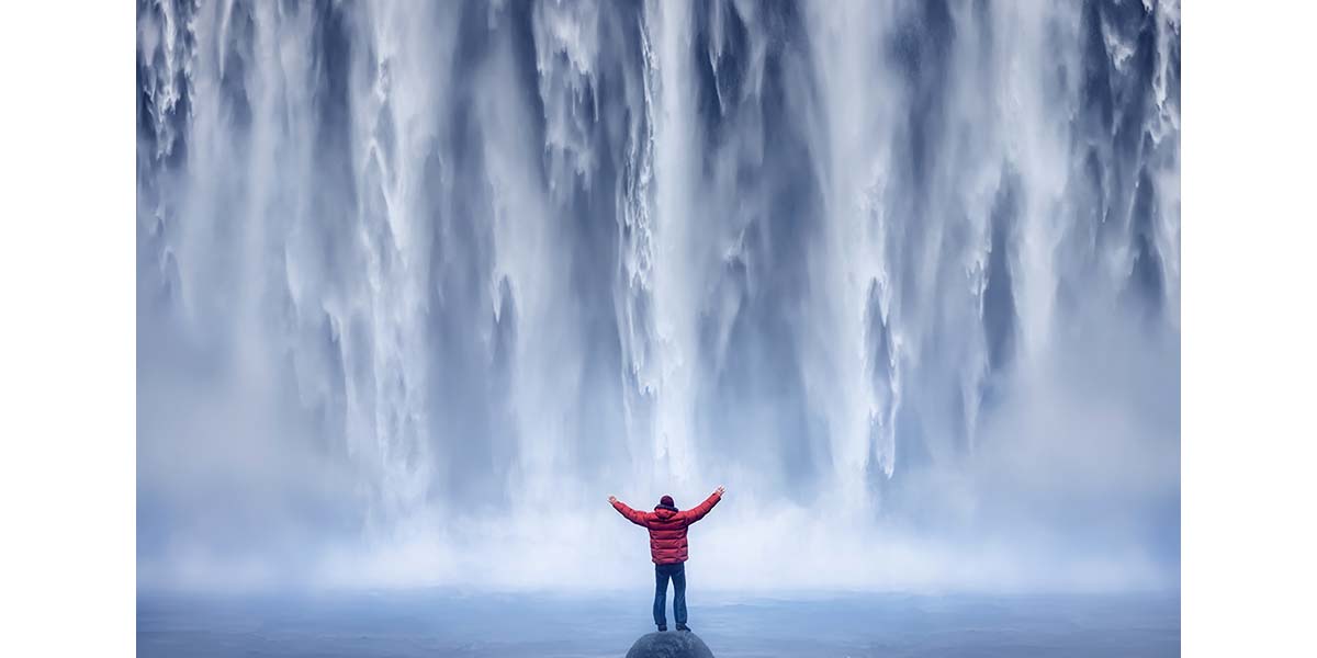 Person standing arms extended in the spray of a great waterfall